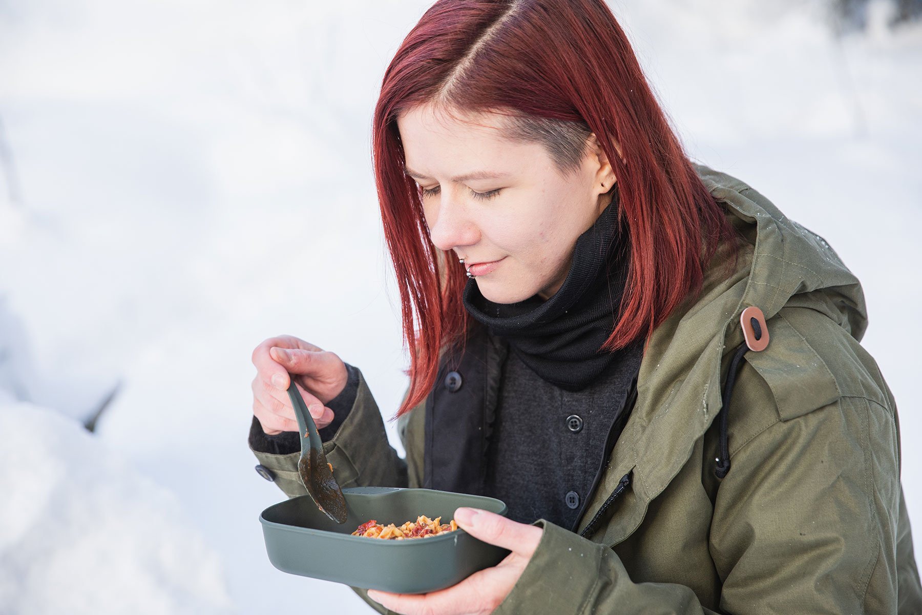 Nainen syö retkiruokaa muoviselta retkeilylautaselta talvella
