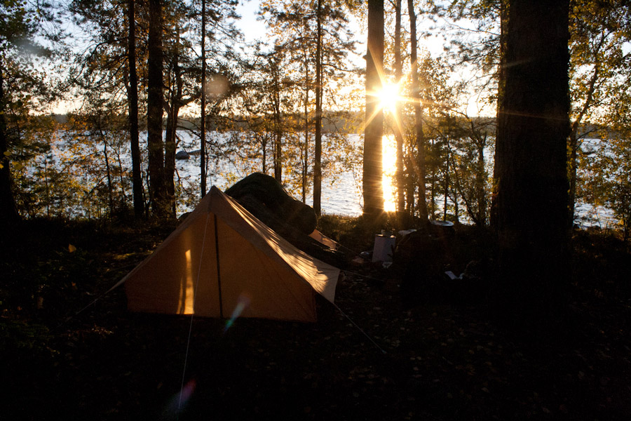 Teltta metsässä järven rannalla aamuauringossa.