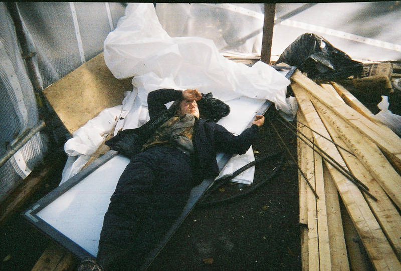 Mies makaa vajassa valkoisen levyn päällä.Taustalla näkyy rakennusmateriaaleja kuten lautaa.