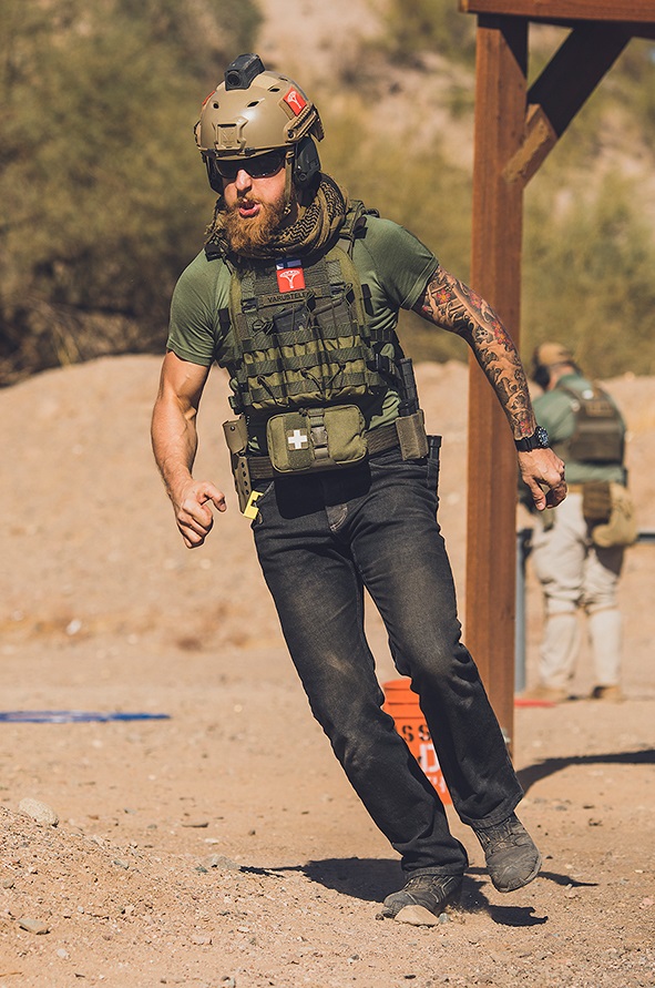 Kypärään, aurinkolaseihin, suojaliiviin, taisteluvyöhön, farkkuihin ja t-paitaan sonnustautunut mies aavikkomaisemassa kääntymässä juoksuaskelin oikealle.