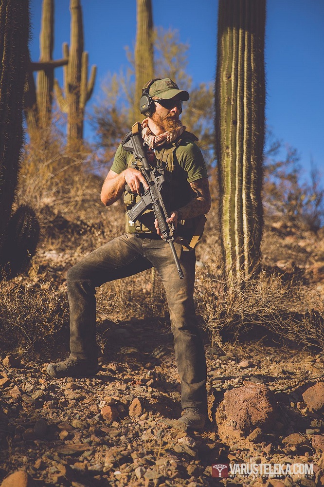 Taistelija seisoo aavikolla pensaiden ja suurten kaktusten ympäröimänä kädessään rynnäkkökivääri.