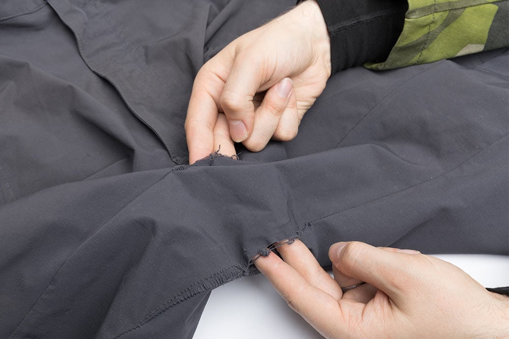 Särmä zip-off housujen haarasaumat, joista molemmista on työnnetty kaksi sormea housujen sisäpuolelle .