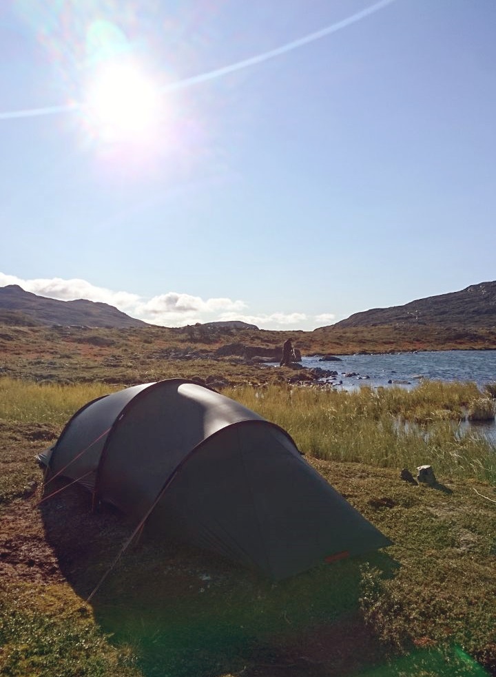 Aurinkoinen telttapaikka veden äärellä.