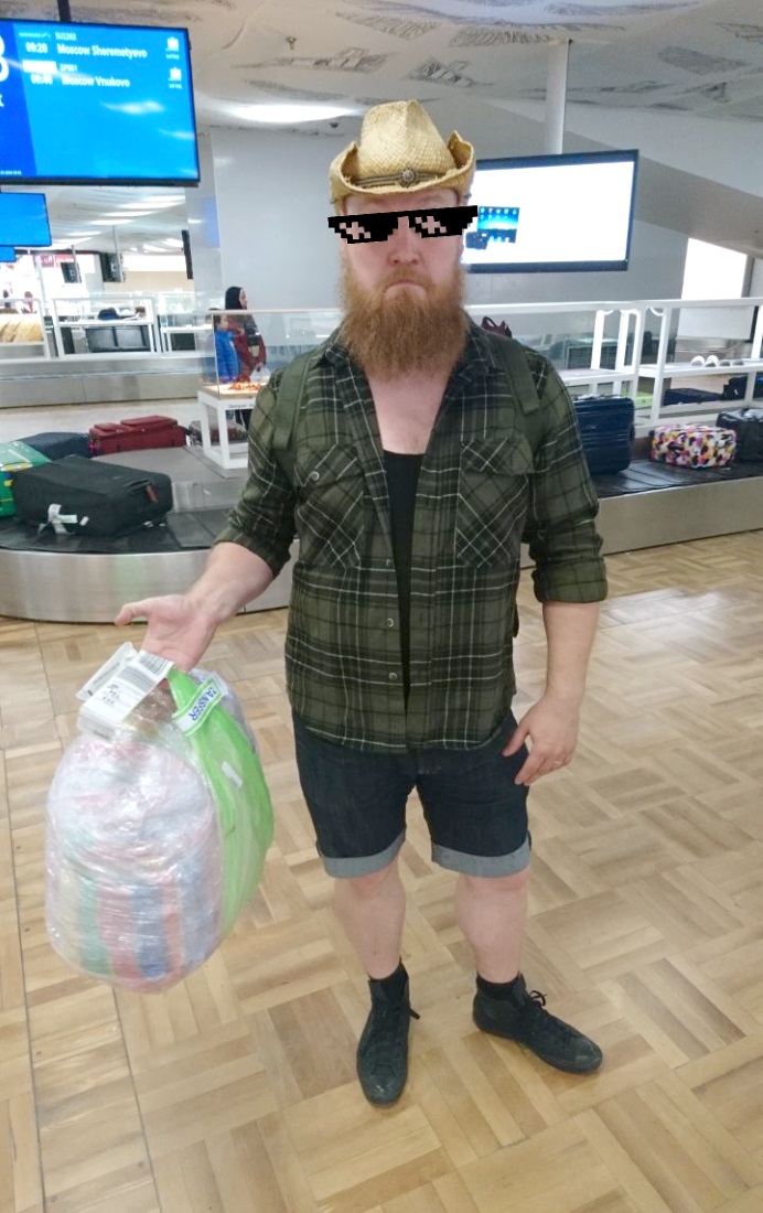 Mies pitää kädessään muoviin käärittyä kestokassia lentokentän matkatavarahihnan edessä.