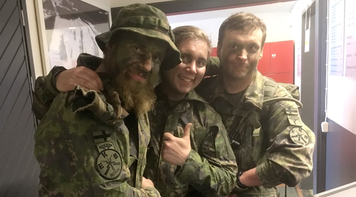 Kolme taistelijaa poseeraa ja hymyilee kameralle käsi kaverin olalla.
