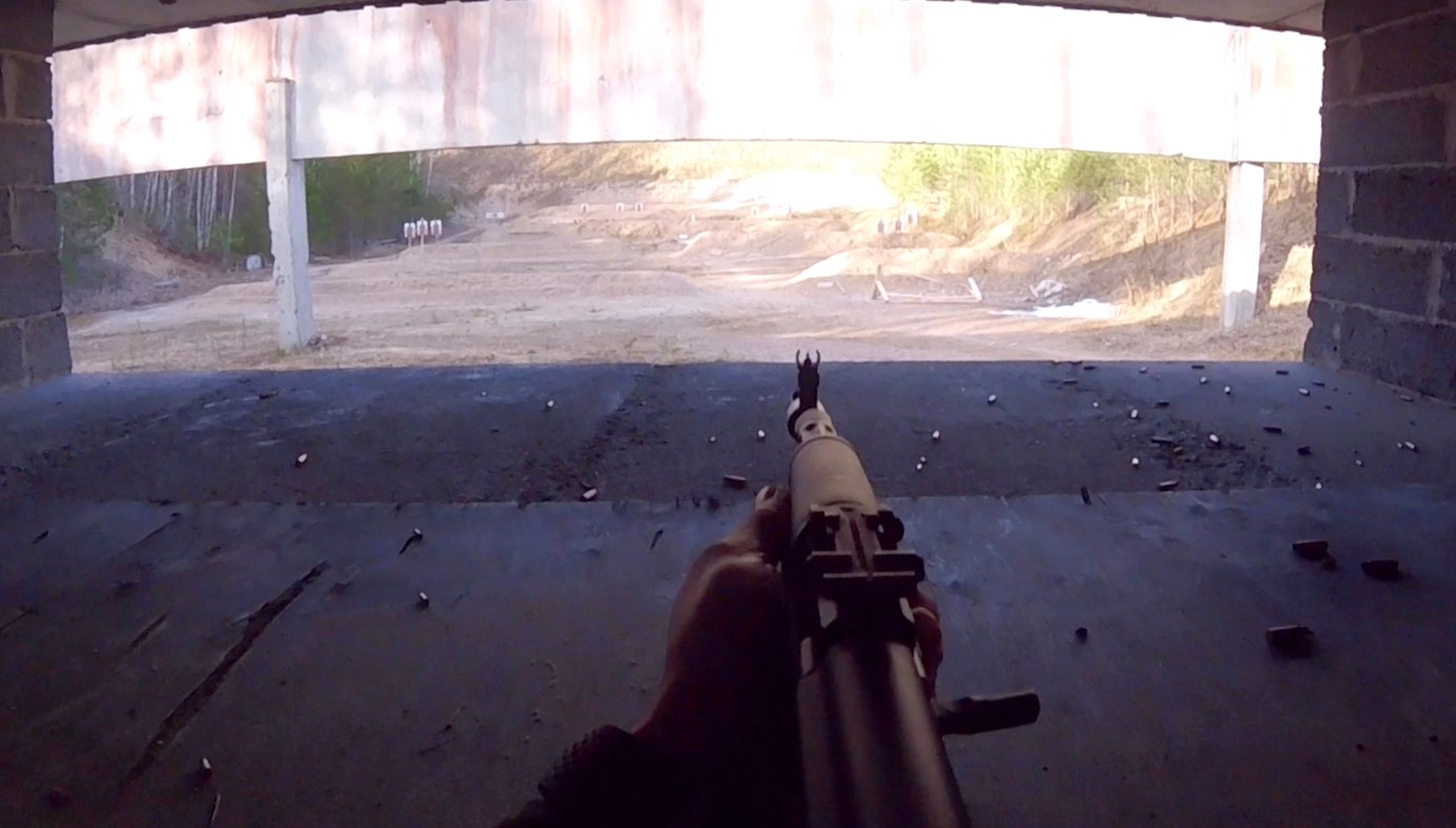 Kivääriradan näkymä ampujan silmin. Edessä ase, jossa päällä tähtäin, kauempana sillan alla maalitauluja.