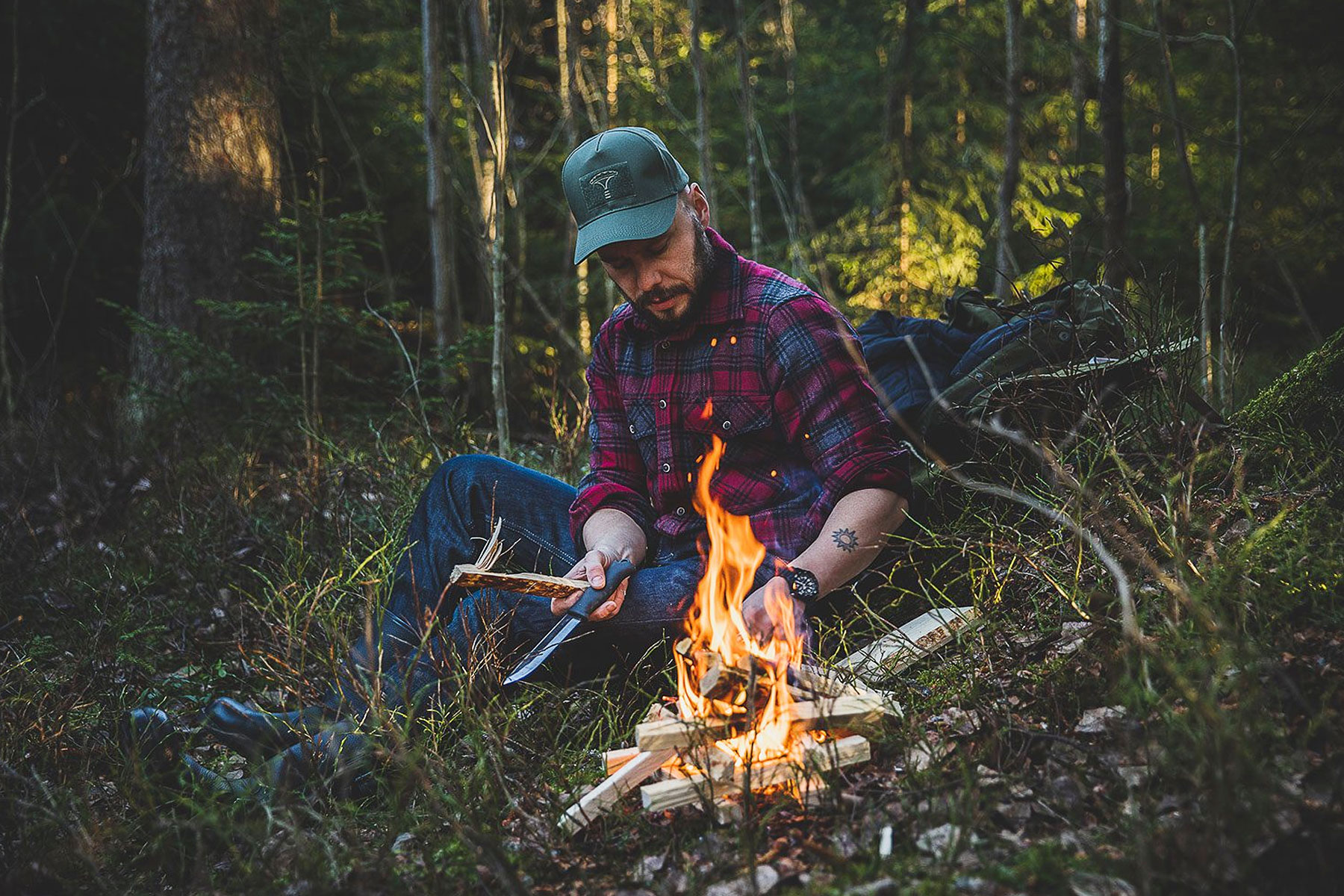 A person lighting a camp fire dressed in Särmä wool flannel shirt.