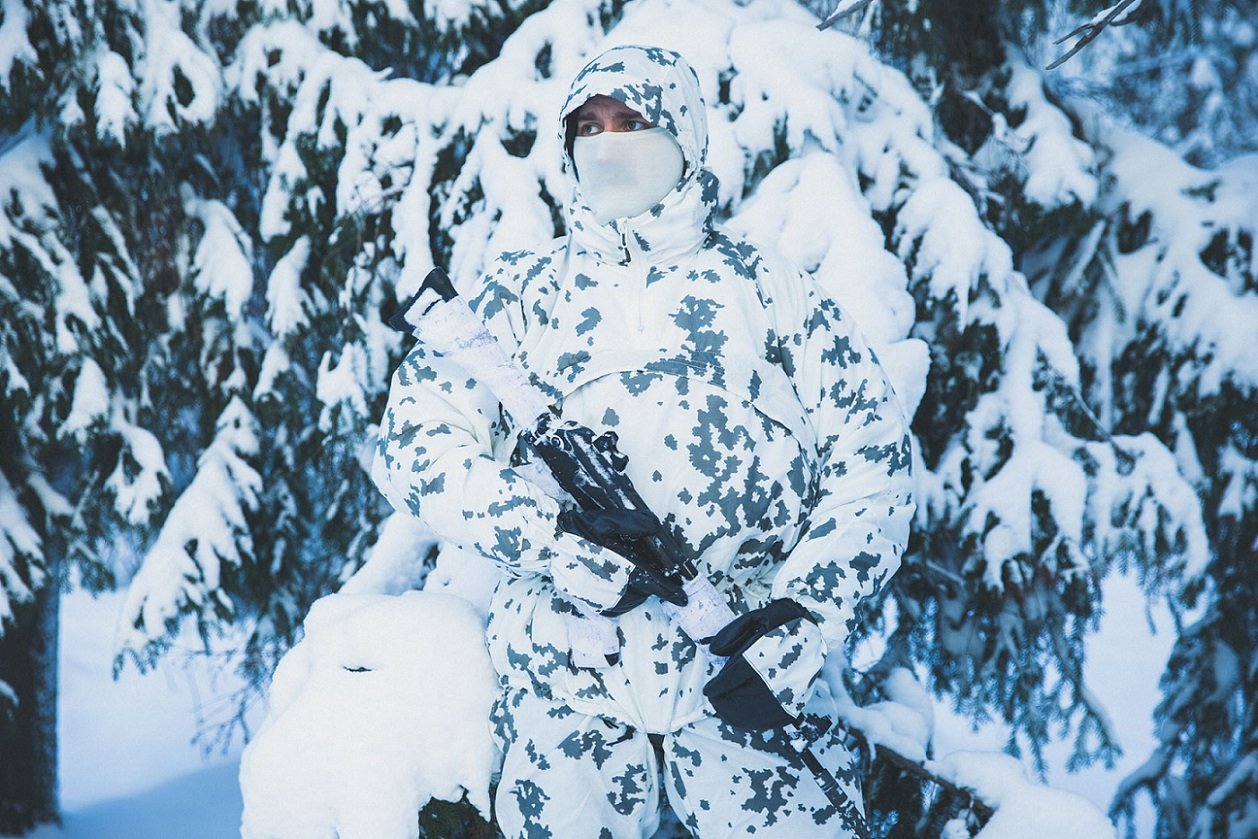 Henkilö talvisessa metsässä pukeutuneena M05 talvimaasokuvioon.