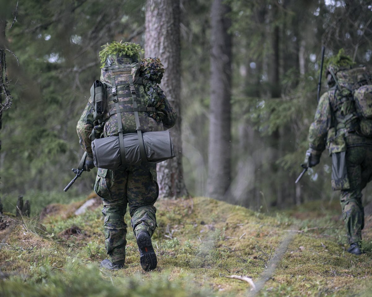 Two soldiers in a forest, the leftmost has Savotta FDF Sleeping pad tied outside the backpack