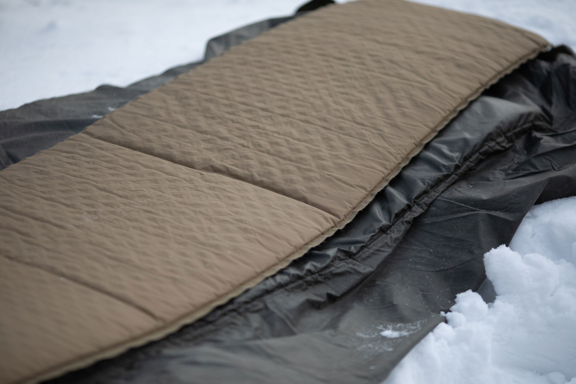 Talvella lumihangessa Savotta SA makuualusta, jonka päällä kevyt ilmatäytteinen makuualusta