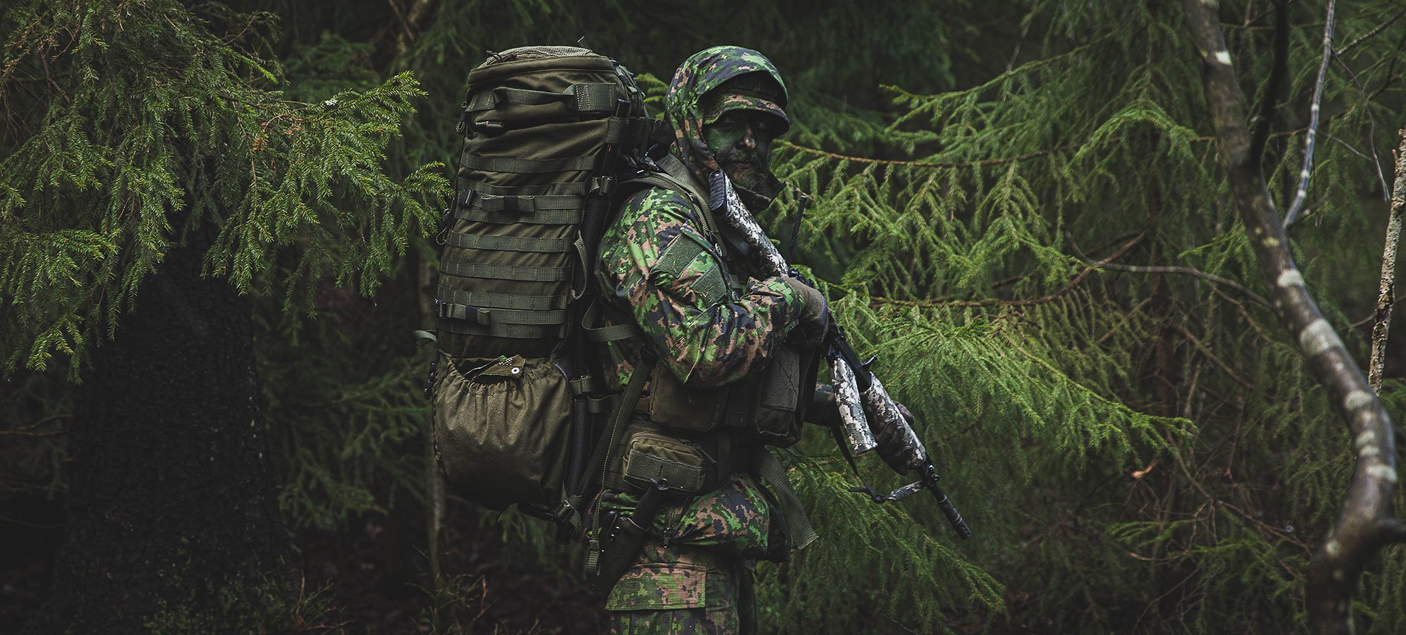 Naamioitunut sotilas metsässä rinkka selässä