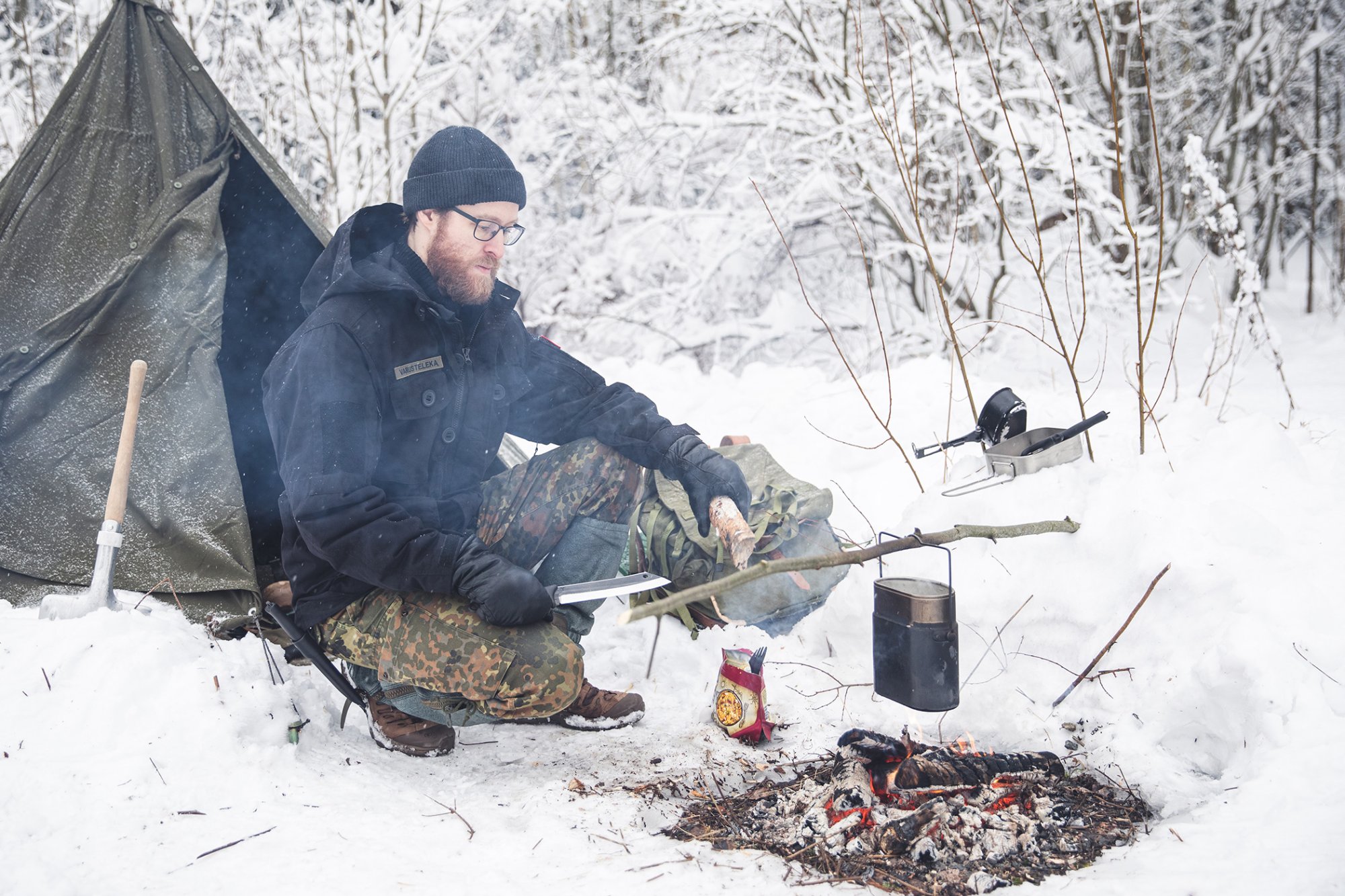 Bushcrafteri laittaa pakissa ruokaa nuotiolla talvisessa metsässä. 