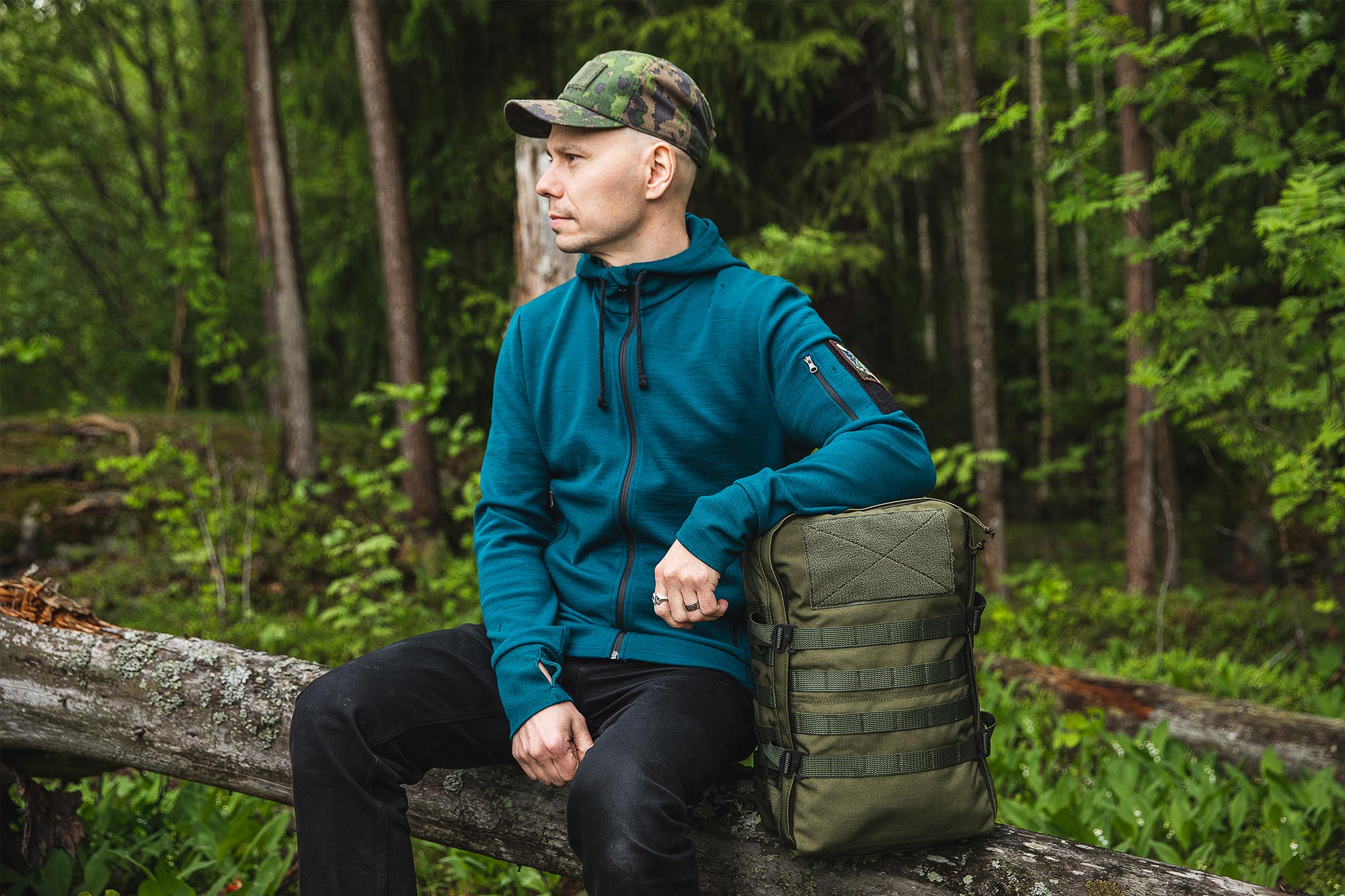 Man sitting in forest wearing Varusteleka Särmä Merino Wool Hoodie 